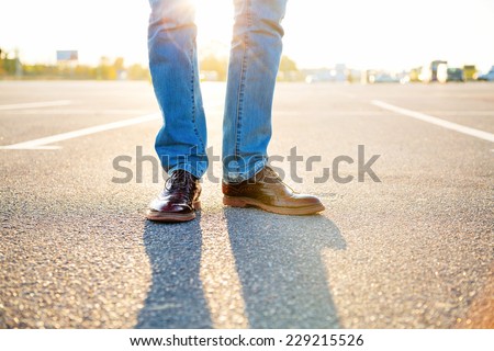 Outdoor fashion image of man legs, wearing jeans and stylish vintage shoes, sunny day, evening sunlight.