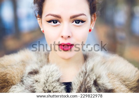 Close up outdoor fashion portrait of beautiful asian girl with perfect skin wearing fur jacket, bright pin up styled make up and eye lenses. Fall outdoor portrait.