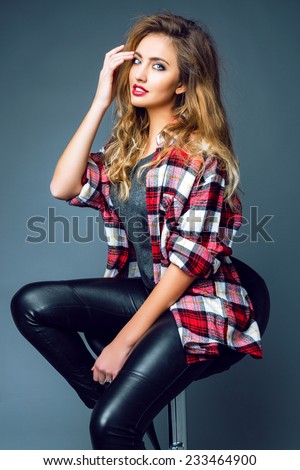Young sexy woman model wearing stylish trendy leather pants and grunge hipster plaid shirt posing at studio, have fluffy blonde hairs and smoky bright make up. Rock n roll fashion style.