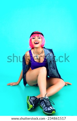 Fashion studio portrait of pretty woman wearing pink party wig bright make up and swag style outfit and sportive sneakers, dance and making funny faces. Bright mint background, not isolated.