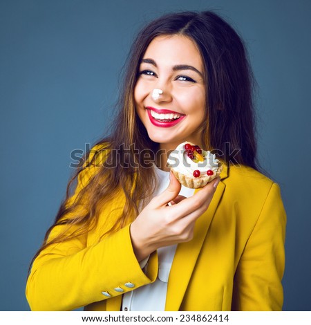Close up funny studio portrait of young cheerful  pretty brunette woman eating tasty cake, soiled cream, smiling and having fun. Positive emotions, bright colors.