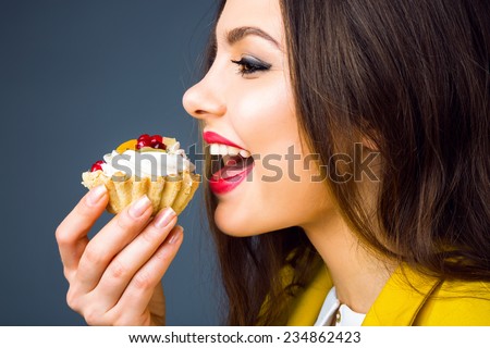 Close up portrait of pretty young brunette woman with bright make up eating tasty cake with berries and cream.