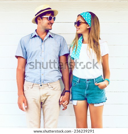 Young couple in love wearing vintage clothing hat and sunglasses, holding hands and posing at white wooden background. Vintage instagram coors.