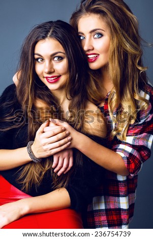 Lifestyle portrait of two sisters hugs and smiling, two stylish girls posing at studio, wearing color matching red and black clothes.