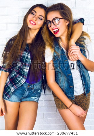 Lifestyle urban bright portrait of two young best friend girls hugs and having fun together. Wearing hipster glasses , bright sexy make up, vintage denim and plaid shirt.
