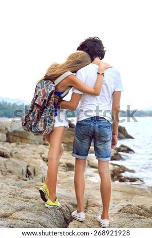 Young stylish couple posing at the beach, travel with backpack, wearing stylish hipster summer clothes and sneakers.