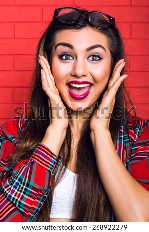 Fashion bright portrait of young woman with amazing long hairs and bright make up,having fun at the room, wearing hipster outfit, red urban wall background. Surprised emotions.