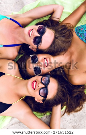 Happy three girls friends laying and getting sunbathe on the beach, close up portrait of stunning smiling women in bikini on vacation.