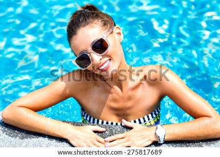 Close up fashion portrait of sexy tanned woman relaxed and swimming at pool. wearing bright bikini and sunglasses, smiling and looking on camera.