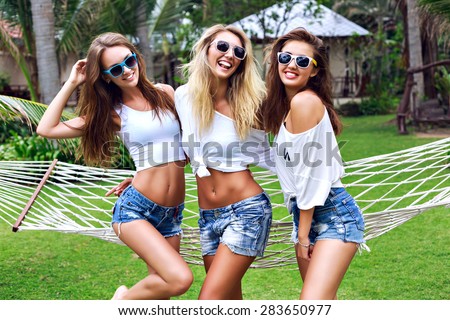 Summer lifestyle portrait of thee hipster stylish women with fit sexy body, wearing denim mini shorts and vintage sunglasses. Girls friends going crazy, having fun, dancing, laughing and screaming.