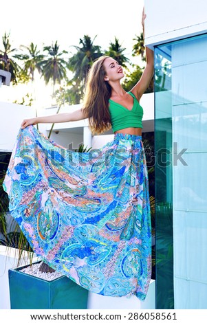 Fashion summer image of stunning brunette woman with sensual face and perfect body, wearing stylish silk skirt which developed in the wind and top, posing at luxury hotel, vacation exotic country.