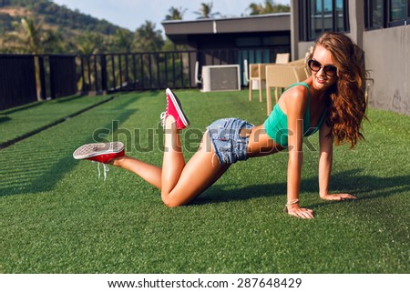Summer portrait of sexy hipster woman, having fun on the roof at tropical island, wearing crop top denim micro shorts and sunglasses, brunette fluffy hairs, urban background.
