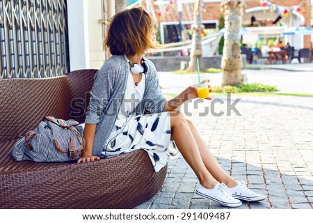 Young beautiful stylish woman, sitting on the street bench, traveling alone, enjoy her free time, wearing vintage hipster trendy outfit, drinking smoothie, enjoy weekends.