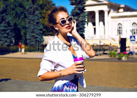 Stylish sexy girl traveling at Europe, drinking tasty latte, enjoy her trip, wearing bright printed summer romper, trendy jewelry and vintage sparkled sunglasses, bright toned colors.