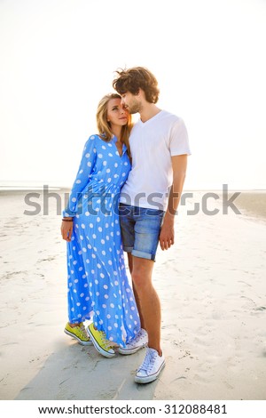 Summer sensual fashion portrait of young couple in love, having fun, relaxed end end enjoy time together at lonely exotic beach, beautiful sunset, elegant trendy clothes, romantic atmosphere.