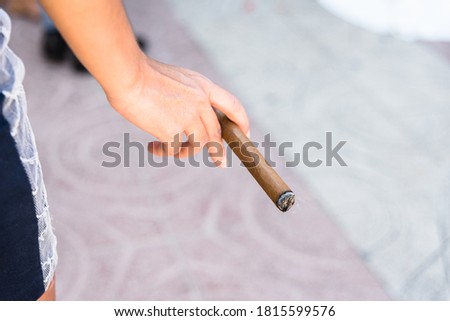 Detail of the hand of a young woman holding a cigar, out of focus background with copy space, defocused.