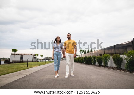 Cheerful twosome is walking down the street. They looking ahead with smile. Copy space. Alley on background