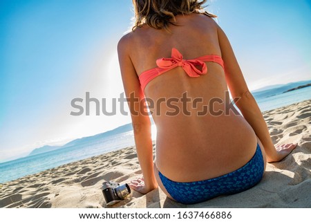 Mujer sentada en una playa de arena con cámara analógica retro.