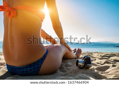 Mujer sentada en una playa de arena con cámara analógica retro.