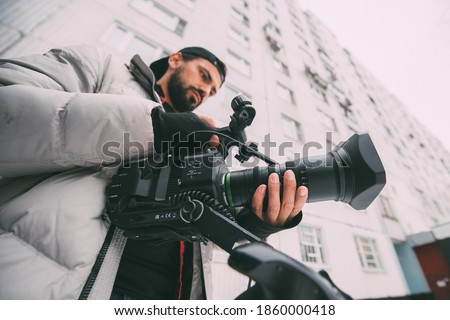 Director of photography with a camera in his hands on the set. Professional videographer at work on filming a movie, commercial or TV series. The filming process on the street, on location
