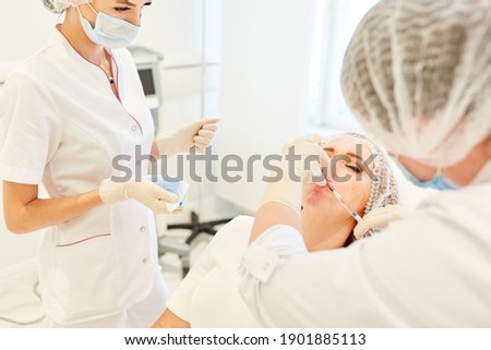 Team of doctors in the beauty clinic injecting hyaluronic acid on the lips as a dermal filler