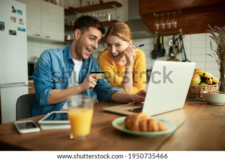 Young happy couple using laptop and credit card while shopping on the internet at home. 