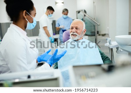 Black female dentist communicating with mature man during teeth exam at dentist's office. Focus is on man.  Foto d'archivio © 