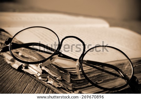 a pair of round-framed eyeglasses on an old book, on a rustic wooden table, in sepia toning and slight vignette added