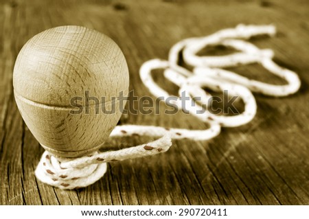 a traditional wooden spinning top with a string coiled in its axis on a rustic wooden surface, in sepia toning