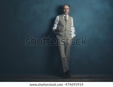 Vintage 1920s businessman with glass of whiskey leaning against wall.