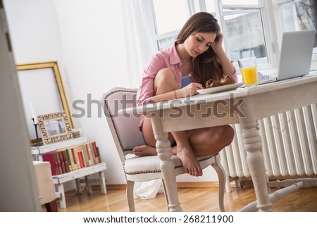 Young female student sitting in her living room and  writing something.Blur and grain added for artistic impression.
