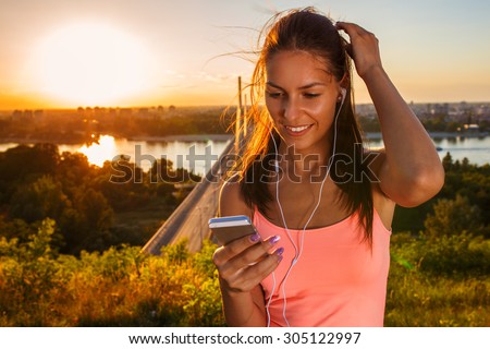 Female jogger running and listening to music on her smart phone.Sunset and lens flare effect.