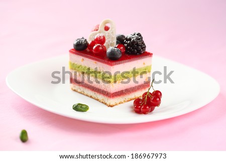 Piece of Multi-layered Berry and Pistachio Mousse Cake, on a white plate and on light pink background.