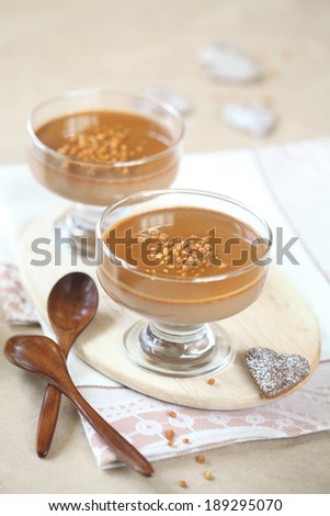 Chocolate Coffee Panna Cotta with Caramel Topping on a wooden cutting board, wooden spoons and chocolate cookies, on a light beige background.