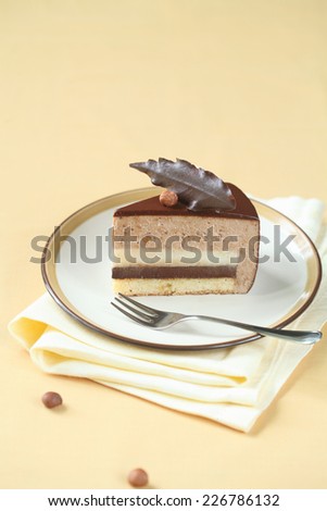 Piece of Chocolate Hazelnut Mousse Cake, silver fork and yellow napkin on yellow background.