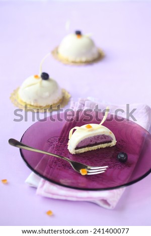 Blueberry and Orange Mousse Cakes decorated with white chocolate curls and toasted coconut flakes, on a purple plate and light purple background.