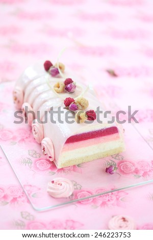 Raspberry Litchi and Rose Yule Log Cake covered with pink glaze and decorated with rose meringue cookies, on a light pink background.