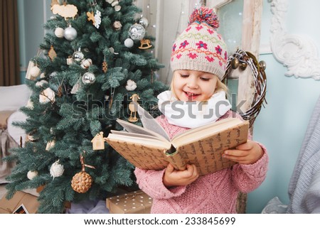 Little girl read the book around the Christmas tree