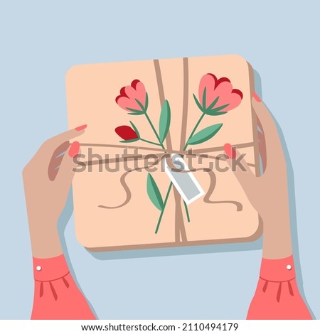 Gift box on the table, top view. The girl is holding a box in her hands. Female hands wrapping a gift in craft paper. The box is decorated with a bouquet of flowers.