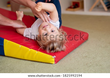 Portrait of a child with cerebral palsy on physiotherapy in a children therapy center. Boy with disability has therapy by doing exercises. Special needs kid has therapy with physiotherapist.