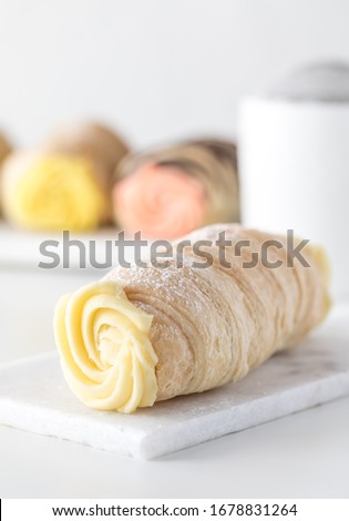 A close up of a creamy cannolo with other cannoli in behind and a powdered sugar sifter against a white background.