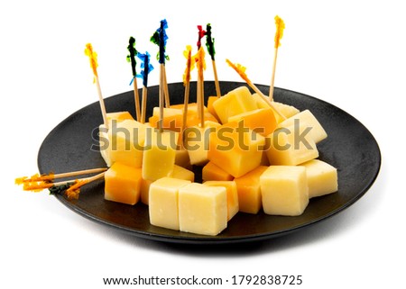 a black plate of orange marble and white cheddar cheese cube appetizers with fancy toothpicks isolated on white