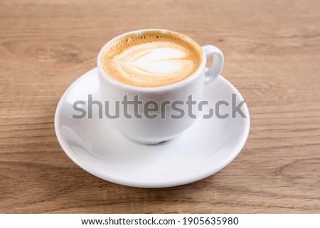 a small white cup and saucer of foamy macchiato coffee on a wooden table