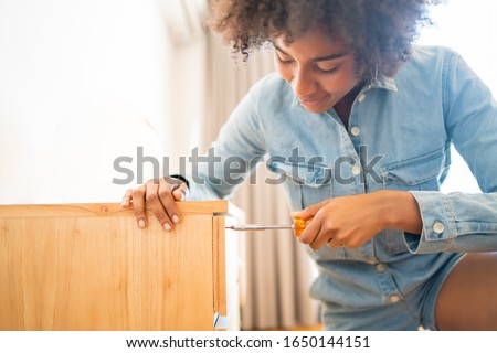 Portrait of young afro woman repairing furniture with a screwdriver at home. Repair and renovation home concept.
