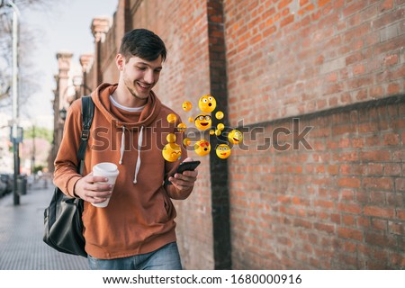 Young man using smartphone sending emojis. Outdoors. Social media concept.