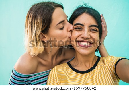 Portrait of lovely lesbian couple having fun and taking a selfie against light blue background. LGBT concept.