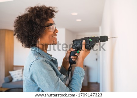 Portrait of young afro woman drilling wall with an electric drill at home. Home improvement concept.