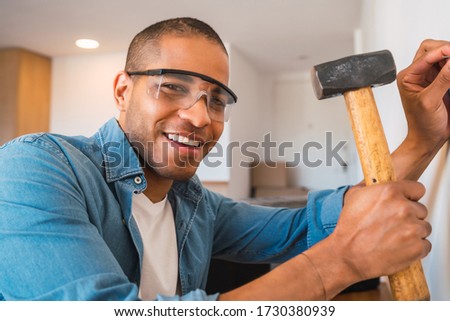 Portrait of young latin man hammering nail on the wall at home. Stay home for renovating house. Lock down and Self quarantine at home. Covid-19.