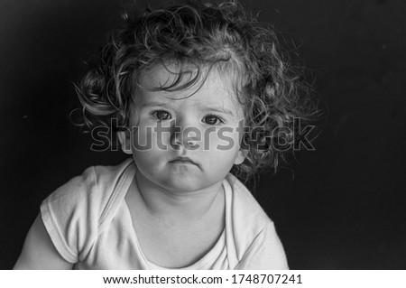 A grayscale portrait of an adorable toddler with curly hair and serious facial expression