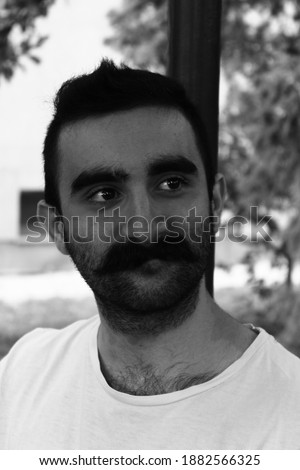 A grayscale portrait of a bearded smiling male looking asiin a park